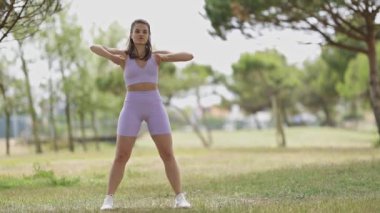 Energetic woman performing a modern dance routine outdoors on the grass in a public park