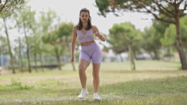 Happy athletic woman in sportswear dancing and playfully falling on the grass in a sunny park