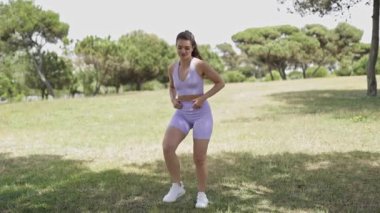 Happy young woman in sportswear dancing and enjoying a sunny day outdoors in a green park
