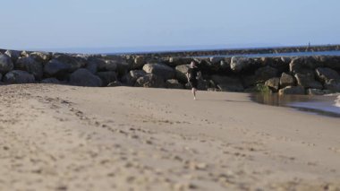 Young athletic man doing his morning cardio workout running barefoot on a sandy beach by the sea