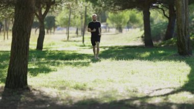 Athletic bearded man running barefoot on green grass in a park for his morning workout