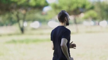 Young man wearing sportswear running barefoot on the grass in a sunny park during his daily workout
