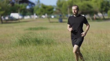 Athletic man with a beard enjoying a barefoot run across a grassy park on a sunny day