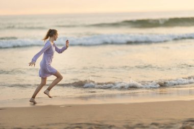 Young girl running joyfully on the beach shoreline during golden hour