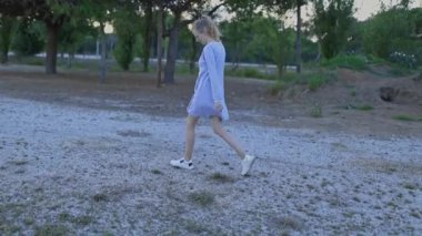 Casual woman walking alone on a gravel path in a green park during a calm afternoon