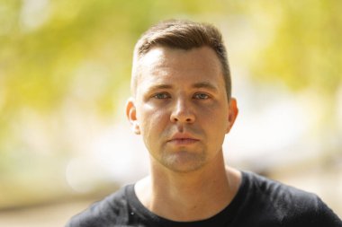 Young man with a neutral expression looking directly at the camera in a natural outdoor setting