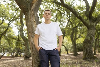 Young man posing for a portrait in a green forest on a sunny day