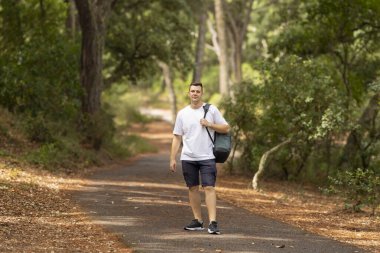Young man enjoying nature walk on scenic park path with green trees
