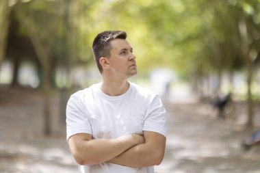 Young man standing outdoors with arms crossed looking away