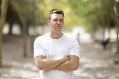 Man standing outdoors with a serious expression, his arms crossed over his chest