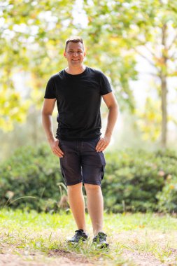 Smiling man standing casually outdoors with hands in pockets on a sunny day