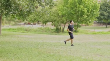 Determined young man jogging on the green grass of a city park during his morning workout routine