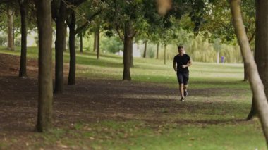 Determined young man in sportswear running through a green park during his morning workout