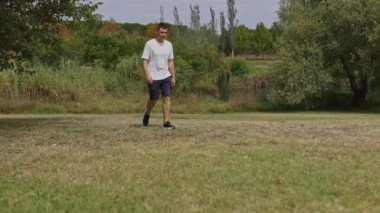 Man in casual clothing walking on a green lawn in a city park on a sunny summer day