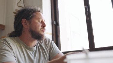 Sakallı ve rastalı, düşünceli orta yaşlı bir adam yemeğini yemeden önce pencereden dışarı bakıyor.