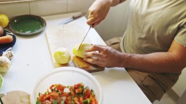 Man carefully cutting potatoes on a wooden board, preparing ingredients for a meal