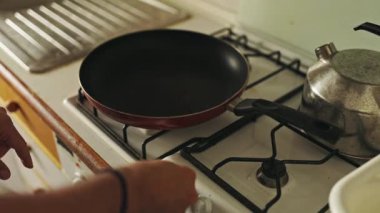 Close up of a hand lighting a gas stove with a frying pan on it, getting ready to cook a meal