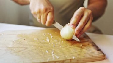 Chefs hands cutting a fresh white onion with a sharp knife on a wooden board