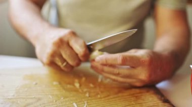 Male chef peeling garlic with a kitchen knife on a wooden cutting board, close up shot