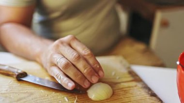Close up of a mans hands chopping a fresh onion with a kitchen knife on a wooden board