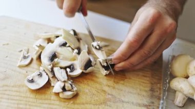 Close up view of male hands slicing fresh button mushrooms with a knife on a cutting board