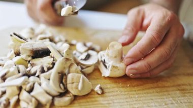 Male hands carefully slicing fresh champignon mushrooms with a knife on a wooden board in a kitchen
