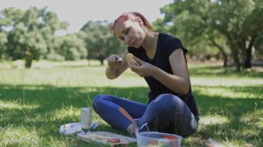 Athletic woman sitting on green grass preparing a healthy lunch sandwich during a sunny day picnic