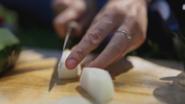 Close up of a womans hands cutting a white onion on a wooden board for a fresh vegetable salad