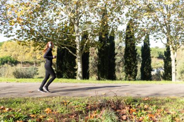 Genç bir kadın yolda koşuyor, kulaklıkla müzik dinliyor.