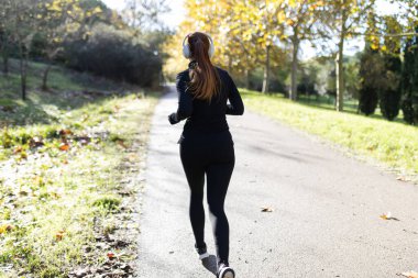 Kadın dışarıda egzersiz yapıyor, kulaklıklarla sonbahar parkında koşuyor.