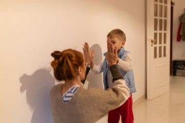 Ebeveyn ve genç çocuk, neşeli bir el çırpma oyununa girişiyor, mutlu bir anı evde paylaşıyorlar.