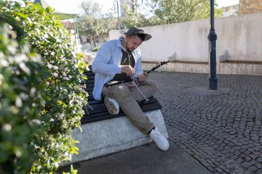 Parktaki bankta oturan bir adam oltaya düğüm atıyor.