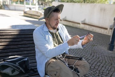 Parktaki bankta otururken küçük mor bir nesneyi birleştirmeye odaklanan adam.