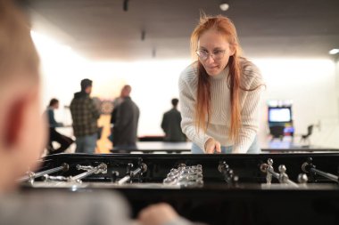 Genç bir kadın sıradan bir eğlence ortamında dikkatle masa futbolu oynuyor.