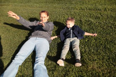 Anne ve çocuk yeşil çimenlerde uzanıyor, güneşli açık havada eğleniyorlar.
