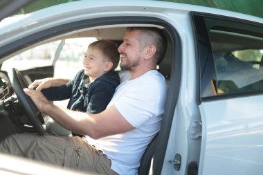 Mutlu baba ve çocuk gülümsüyor, araçta sürüş dersinin keyfini çıkarıyor.