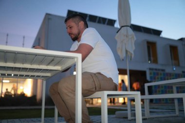 Alacakaranlık saatlerinde modern bir açık hava masasına odaklanmış bir adam.