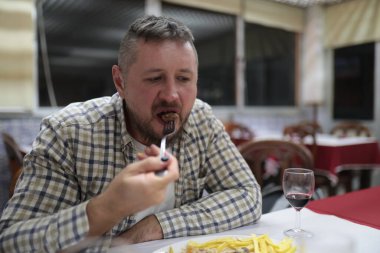 Akşam yemeğinin tadını çıkaran, yemek sırasında çataldan yemek yiyen bir adam.