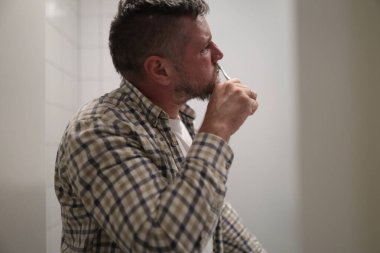 Yetişkin bir adam günlük ağız sağlığı için banyoda diş fırçalıyor.