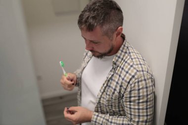 Diş fırçası tutan adam banyoda dişlerini fırçalamaya hazırlanıyor.