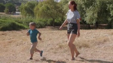 Genç bir kadın ve küçük oğlu güneşli bir günün tadını çıkarıyor, parkta birlikte koşuyorlar.