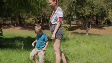 Genç bir aile, anne ve oğul, yeşil bir parkta güneşli bir günde yürüyor ve eğleniyorlar.