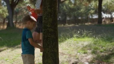 Genç bir çocuk ve annesi bir açık hava sanat kurulumu için bir ağaca turuncu bir ip sarıyorlar.