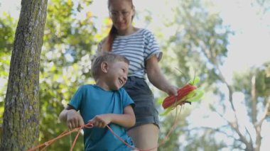 Anne olarak mutlu bir aile eğlencesi küçük oğlunun parktaki parlak bir uçurtmanın ipini çözmesine yardım eder.