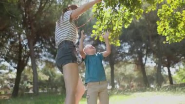 Mutlu anne ve küçük oğlu birlikte oynuyorlar. Güneşli bir parkta zıplıyorlar ve gülüyorlar.