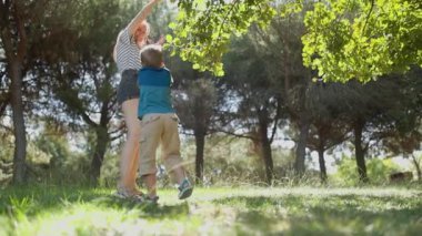 Genç anne ve küçük oğlu güneşli yeşil bir parkta oyuncakla oynarken eğleniyorlar.