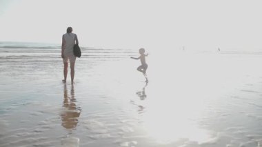 Mutlu anne ve oğul yaz tatilinin tadını çıkarıyor, deniz kıyısındaki ıslak kumda yalınayak yürüyor.