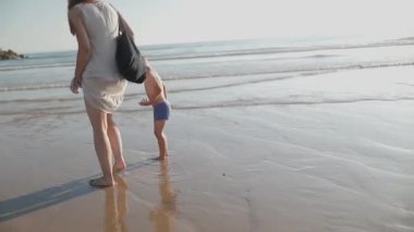 Genç anne ve küçük oğlu güneşli bir yaz akşamı deniz kenarında yürüyüş yapıyorlar.