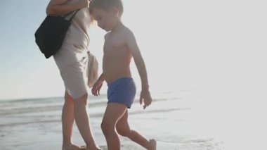 Mutlu küçük çocuk ve annesi güneşli bir yaz gününde deniz dalgalarında oynayıp sıçrıyor.