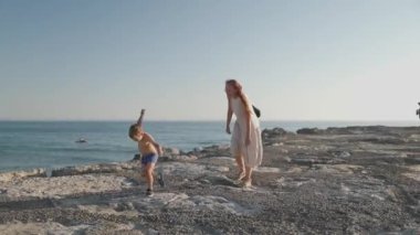 Genç anne ve mutlu oğlu gün batımında kayalık bir sahil kenarında birlikte vakit geçiriyorlar.